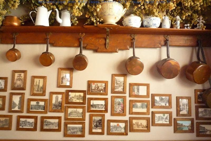 Des casseroles de cuivre suspendues sous une étagère, au-dessus d'un mur de gravures encadrées